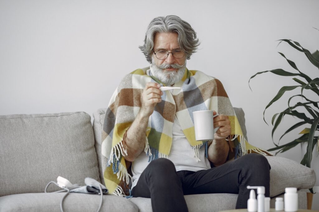 Elderly man checking his temperature while sick with flu-like symptoms