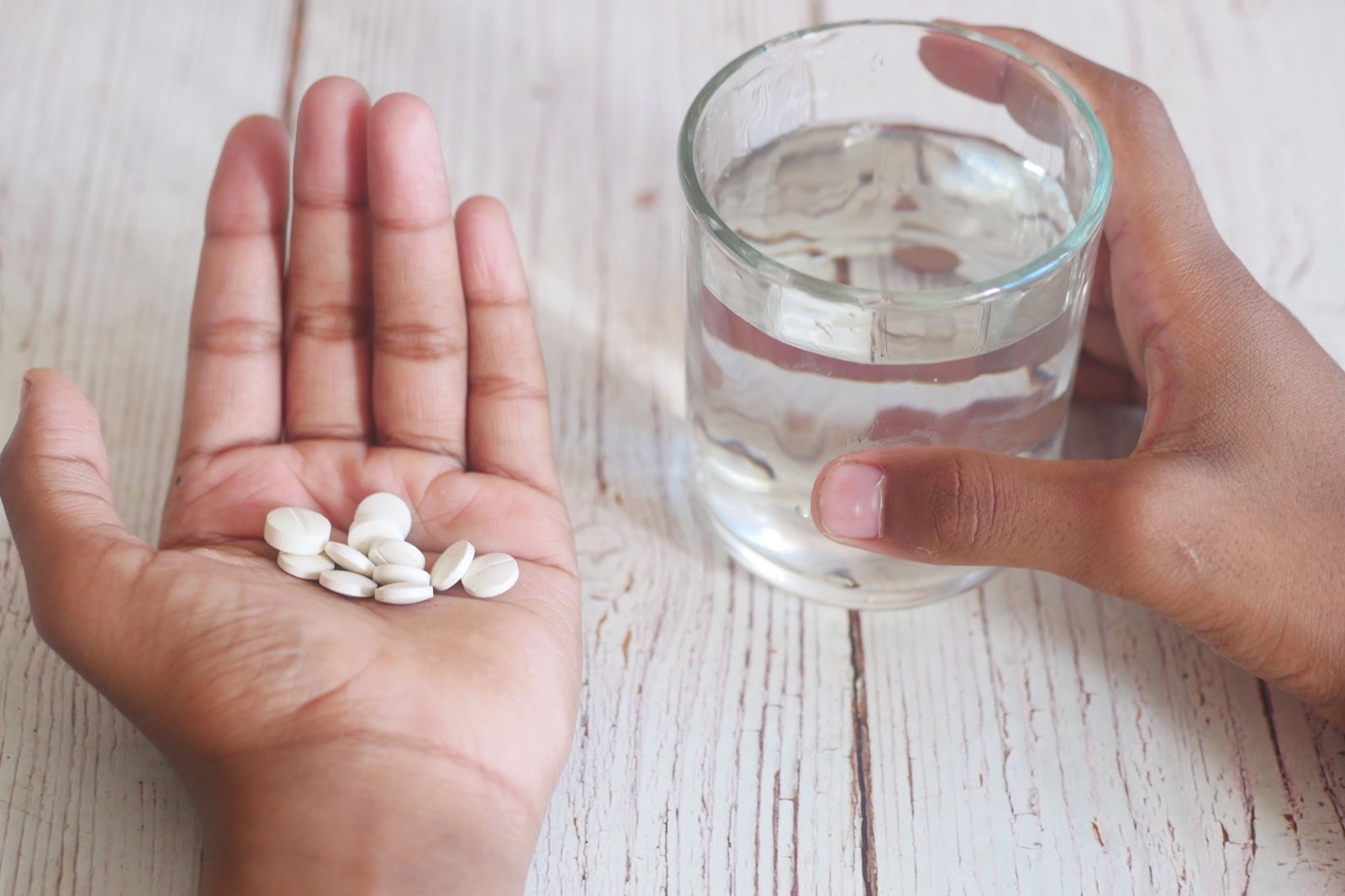 Hands holding medication tablets with a glass of water
