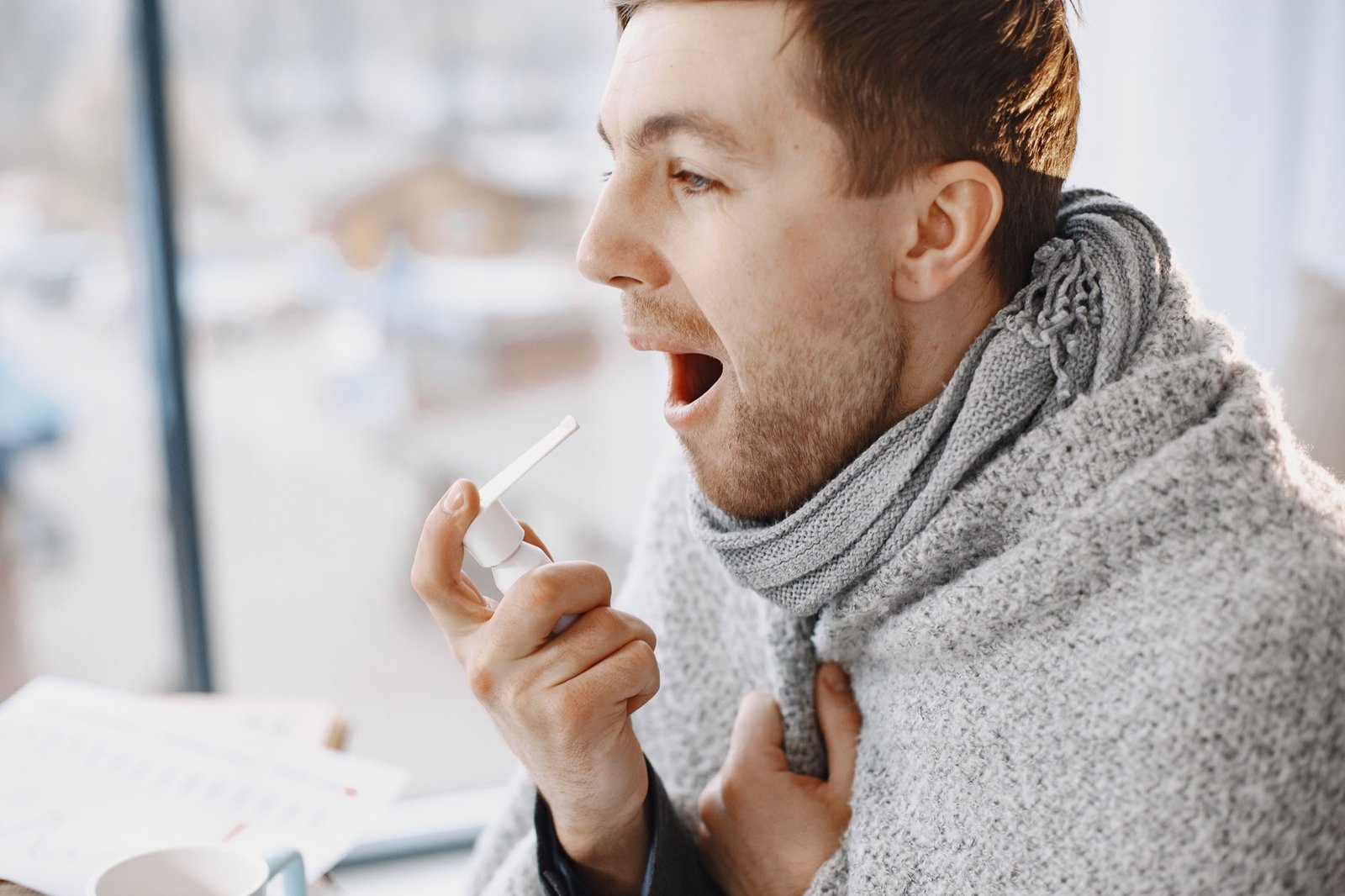 Man using a throat remedy while wrapped in a blanket, feeling unwell