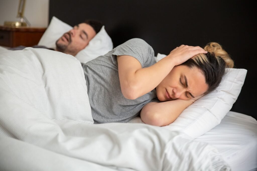 Woman lying awake frustrated while her partner snores beside her