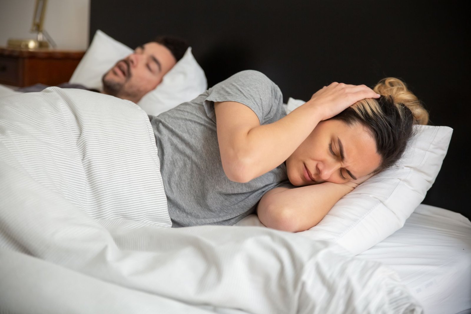 Woman lying awake frustrated while her partner snores beside her