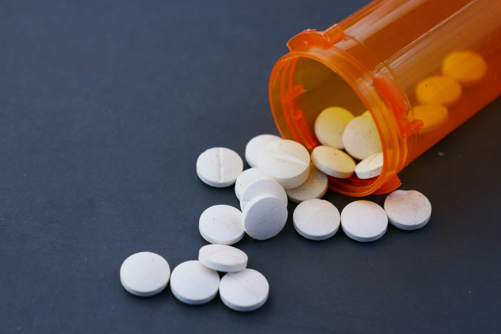 White tablets scattered next to an orange prescription bottle