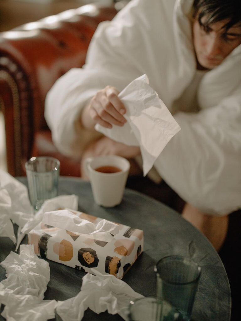 Man wrapped in a blanket with tissues, feeling sick with a cold