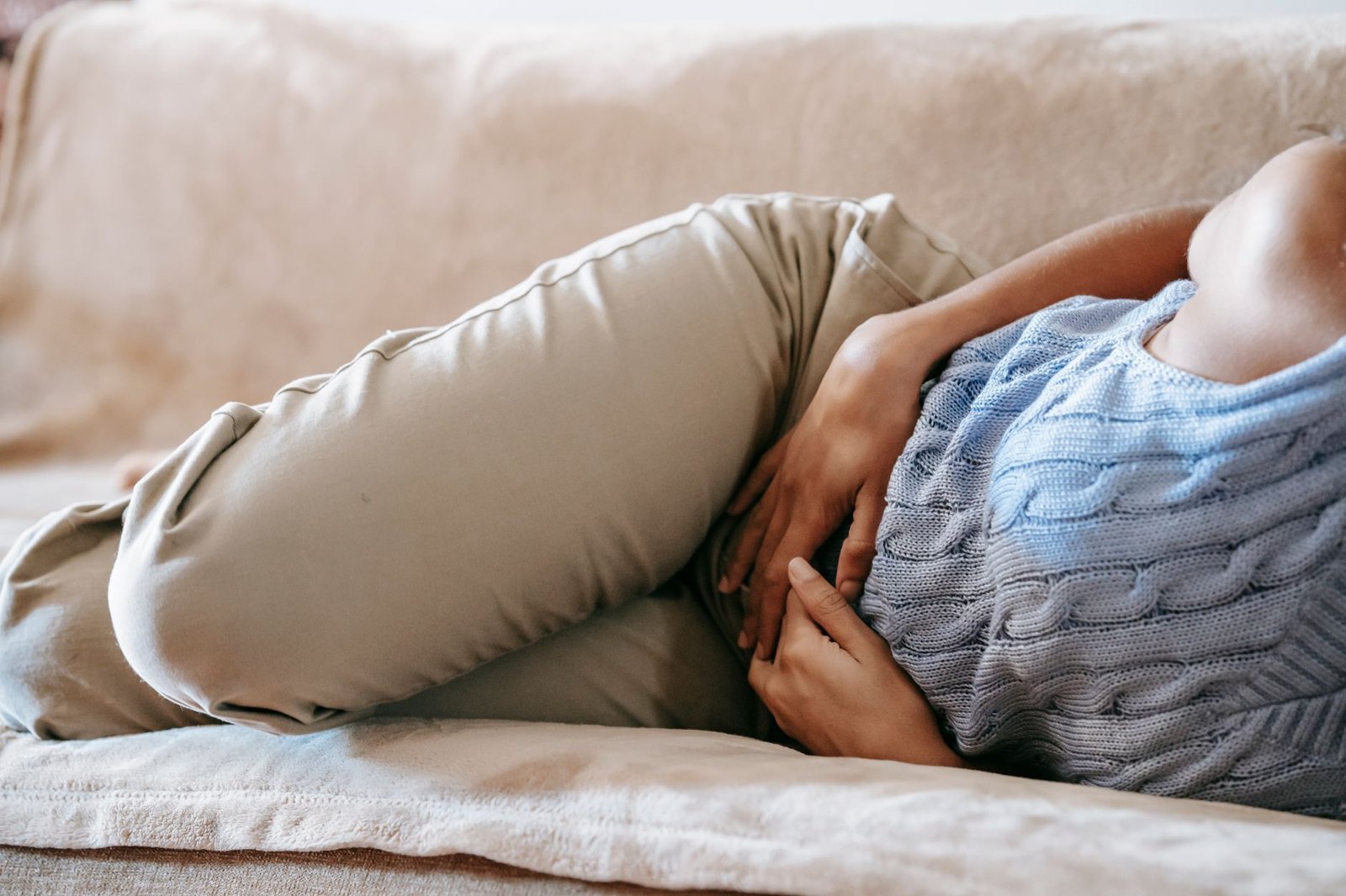 Woman lying on a sofa holding her stomach in discomfort
