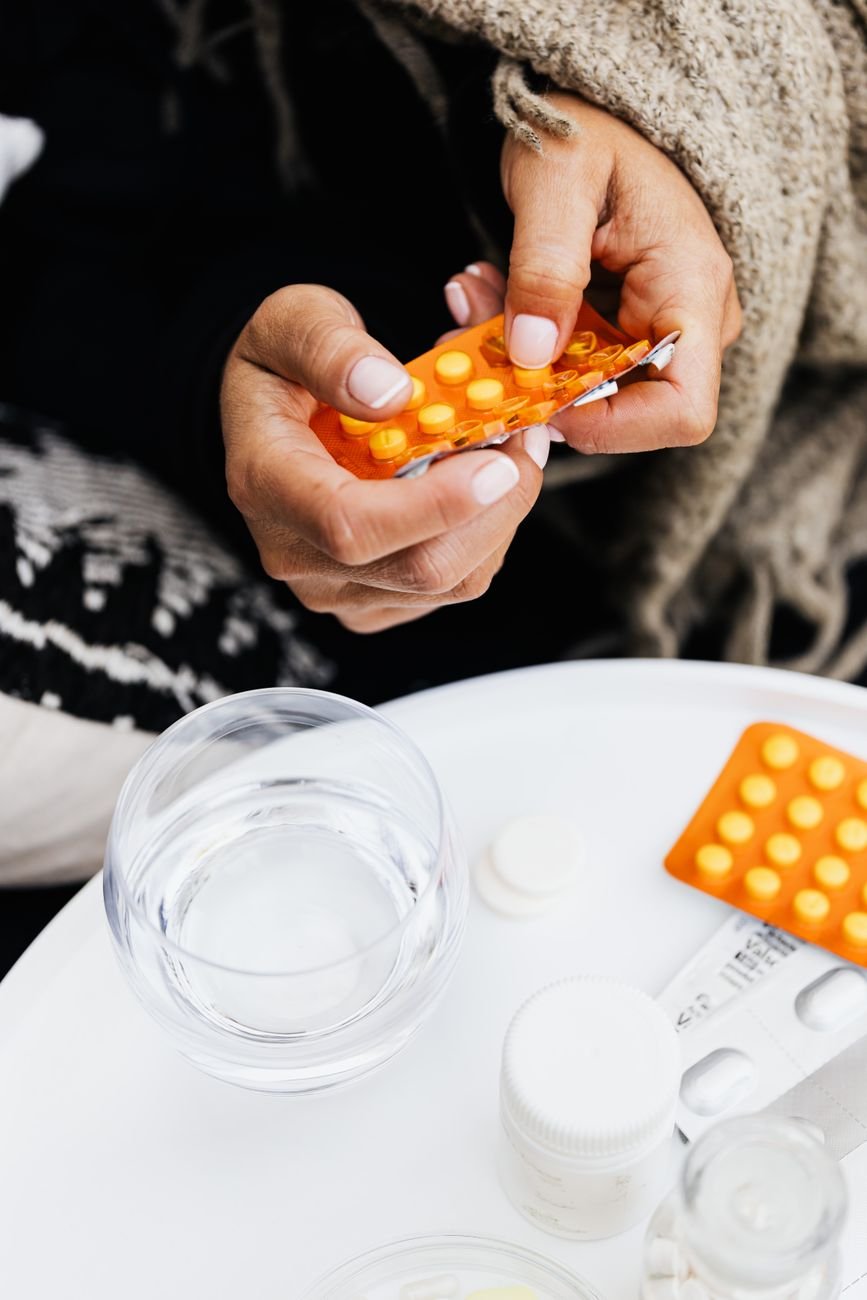 Hands holding a blister pack of tablets next to a glass of water