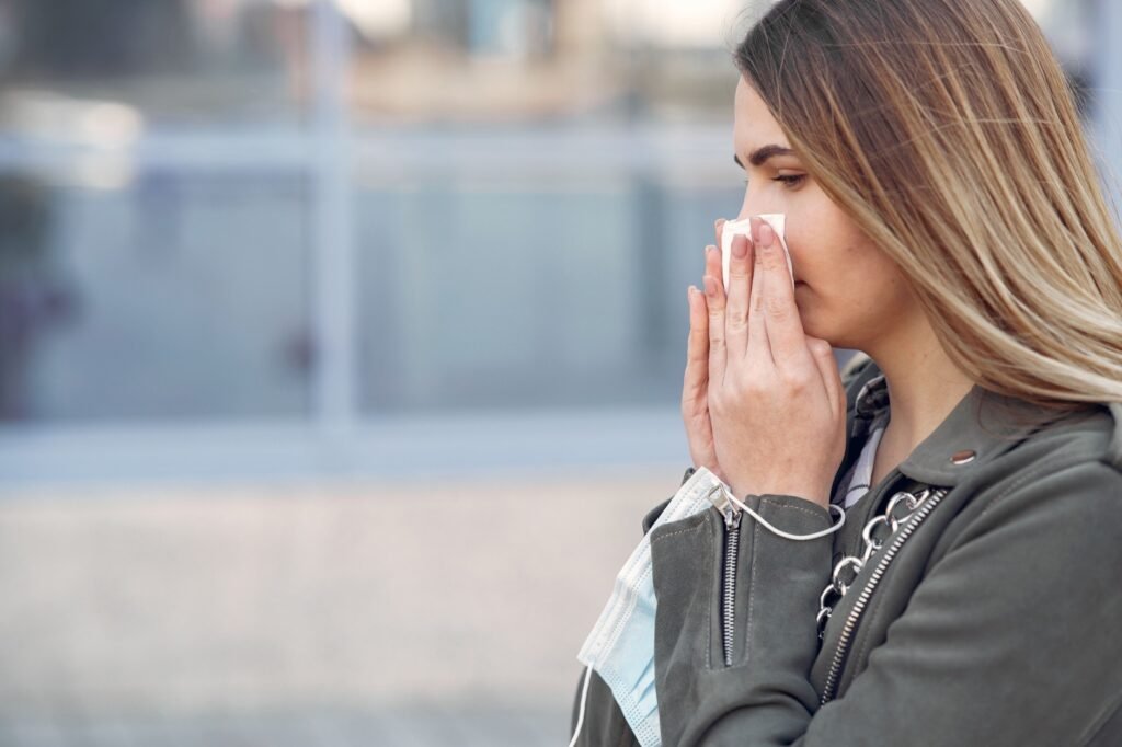Woman sneezing outdoors during pollen season, a common trigger for seasonal allergic rhinitis