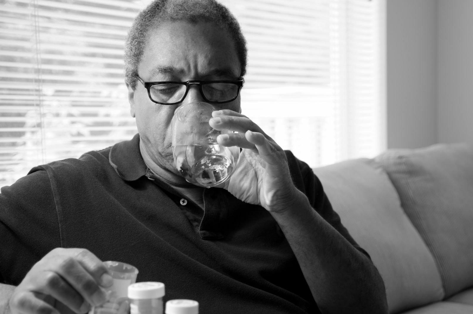 Man on a couch drinking water beside pill bottles, taking acetaminophen for hemorrhoids as directed