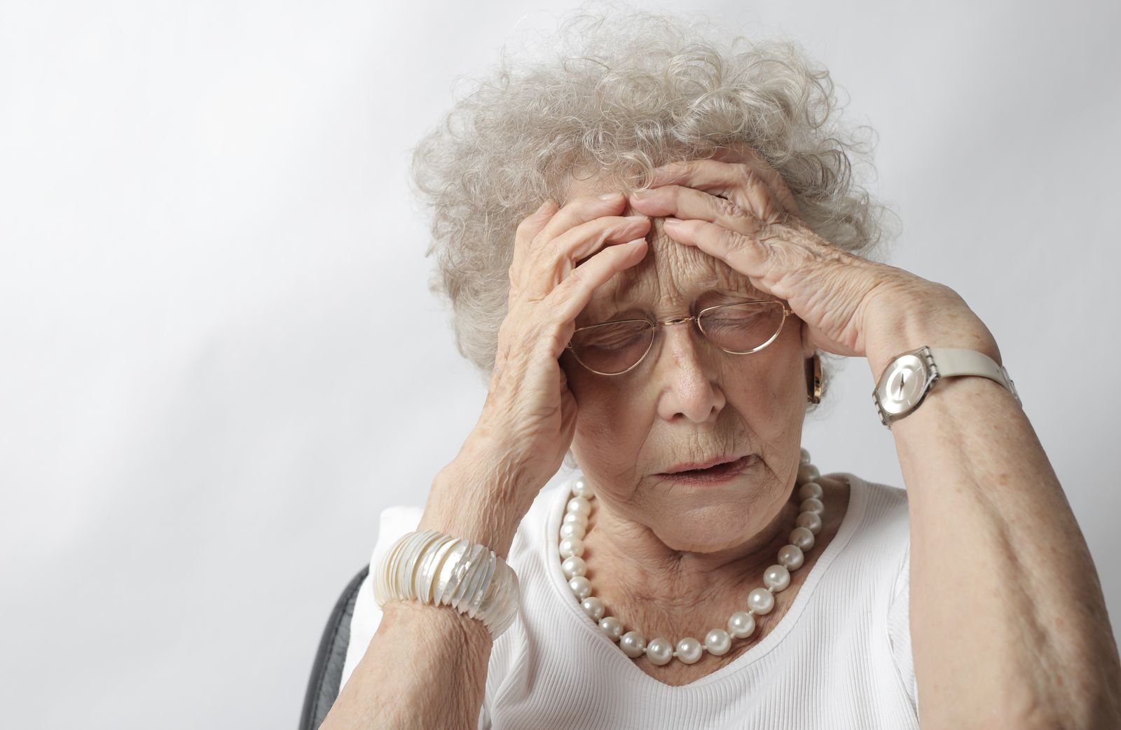 Older woman with her hands on her head from a headache, a common side effect when learning how to apply nitroglycerin ointment for fissures