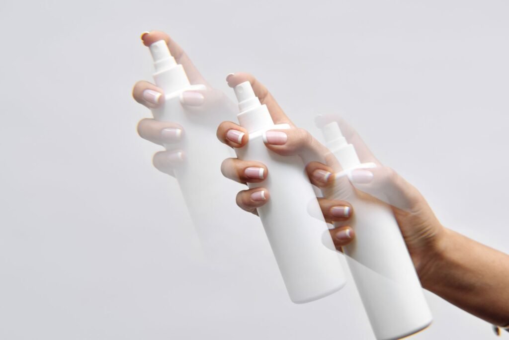 Hands holding plain white spray bottles, representing the no-touch format of Preparation H spray