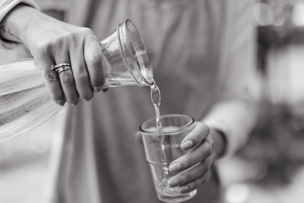 Hands pouring water from a carafe into a glass, a reminder to take Konsyl psyllium fiber with plenty of water