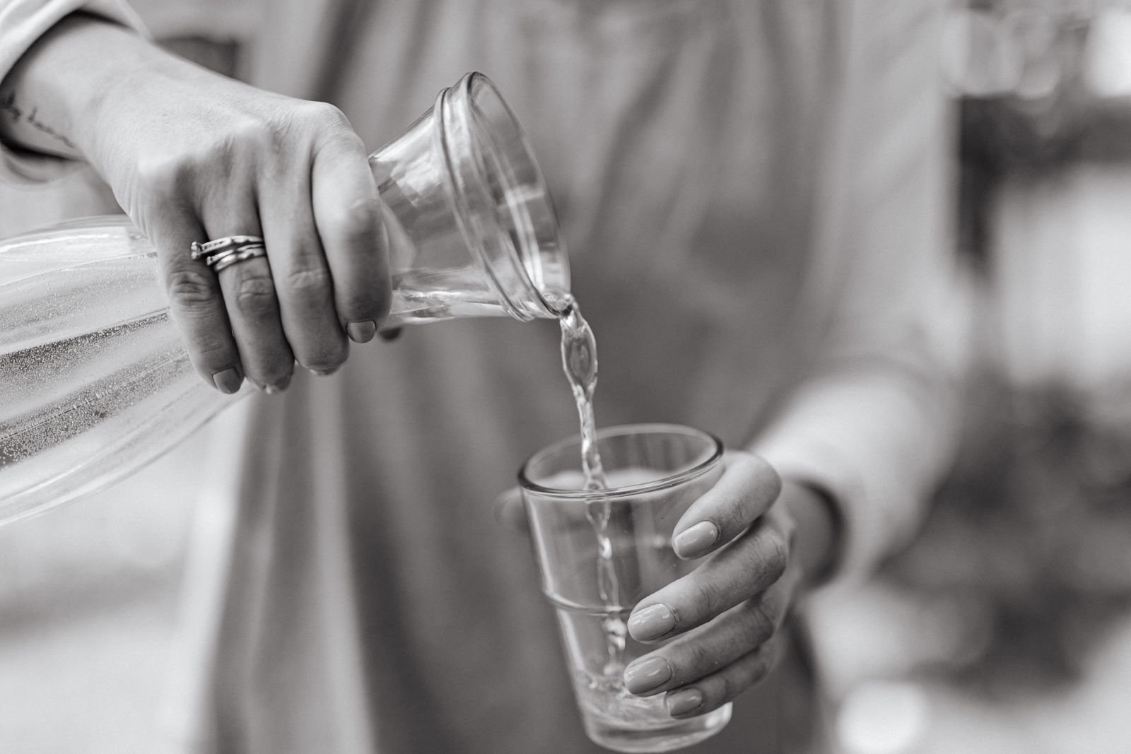 Hands pouring water from a carafe into a glass, a reminder to take Konsyl psyllium fiber with plenty of water