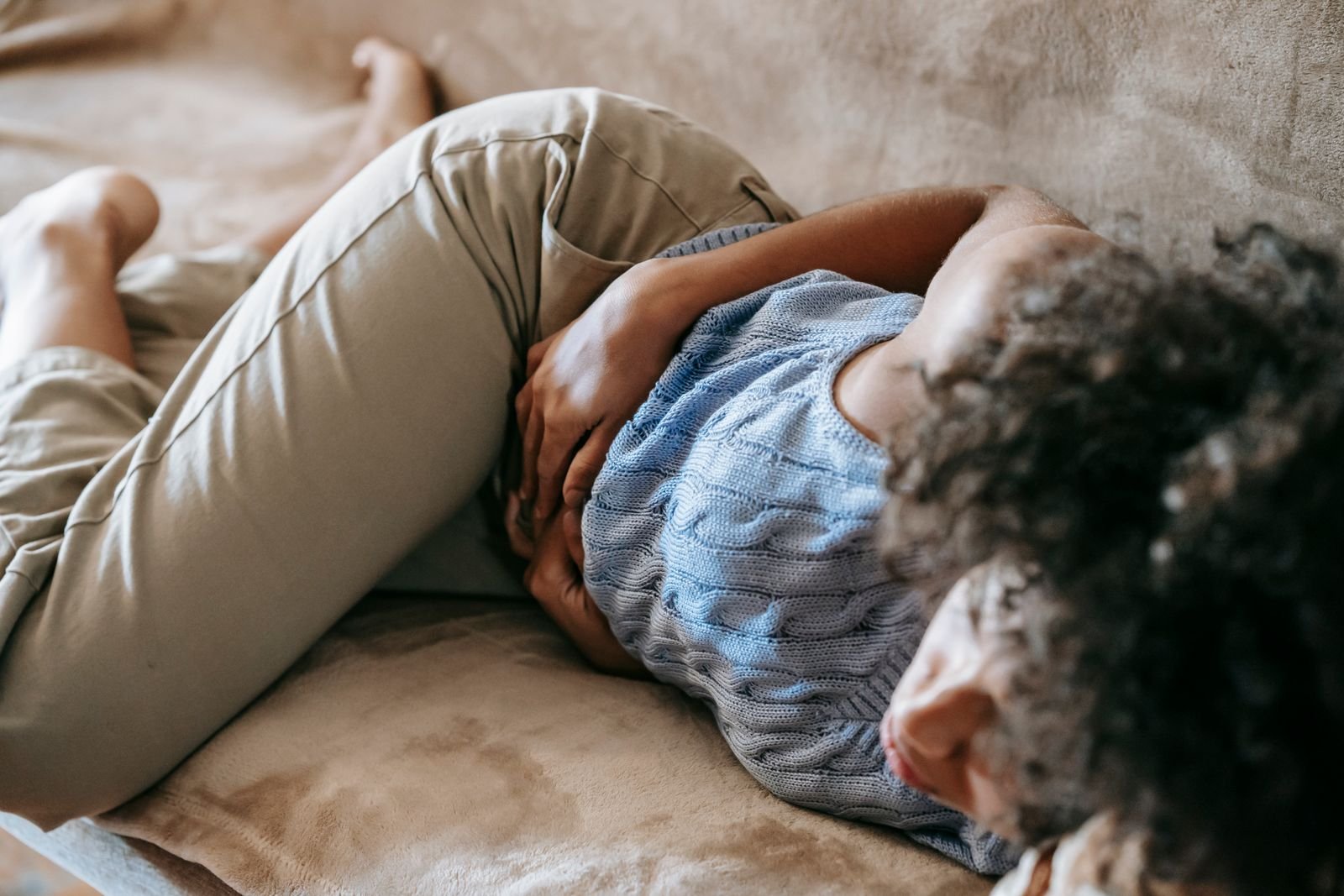 Person lying on a couch in discomfort, a situation where hemorrhoids vs anal fissures symptoms can be hard to tell apart