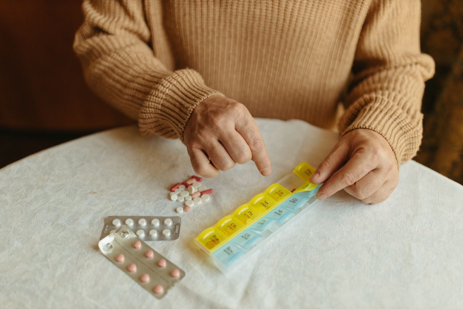 Older woman filling a weekly pill organizer at a table, building a daily routine that answers why take Colace at night