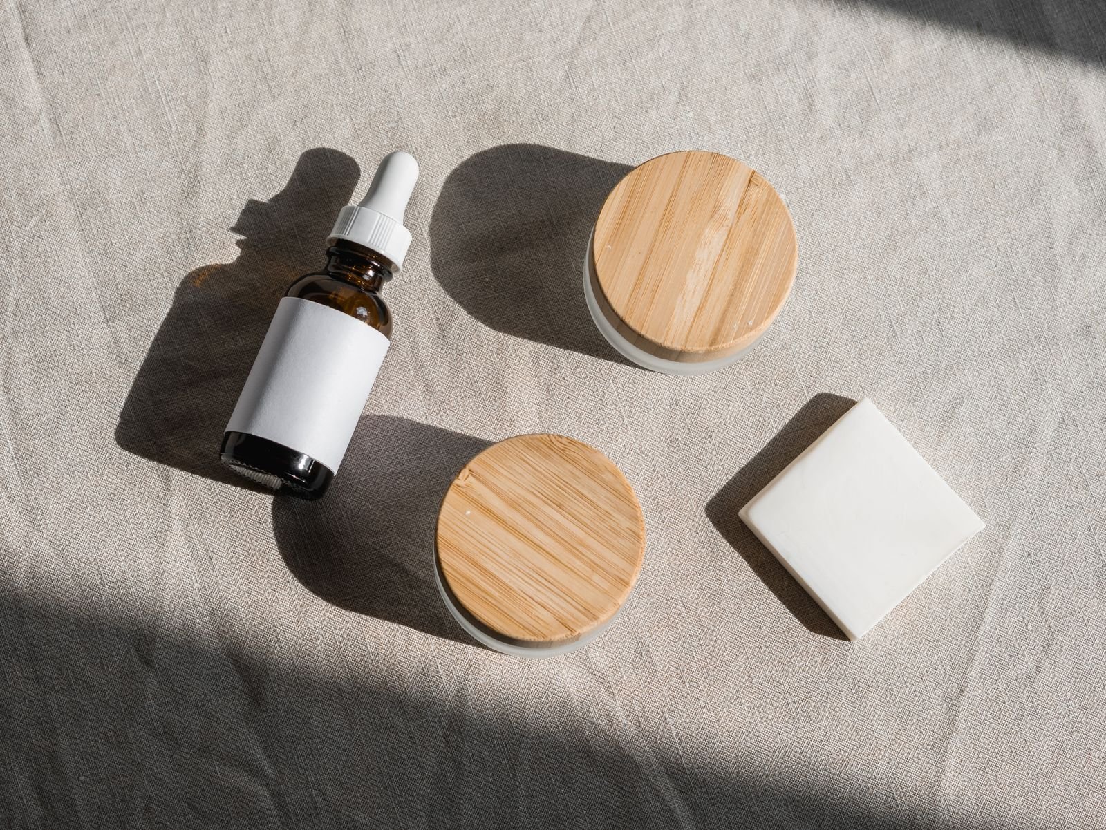 Small jars with wooden lids and a dropper bottle on linen, illustrating the texture choice in Preparation H cream or ointment