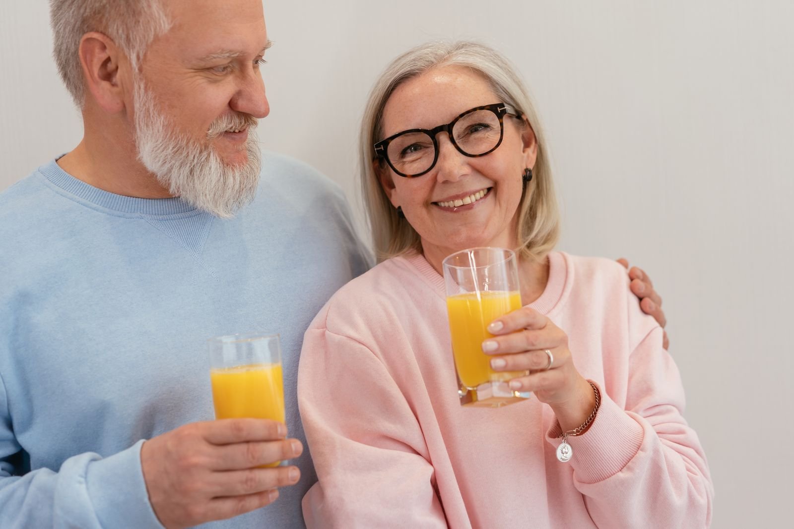 Smiling older couple holding glasses of an orange drink, a familiar way to take a daily fiber supplement