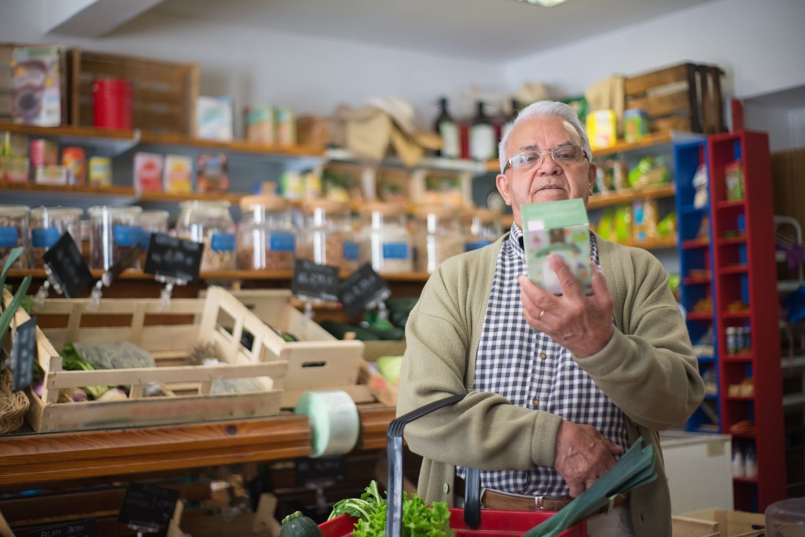 Older man reading a product label in a shop, checking for docusate sodium when choosing a Colace generic