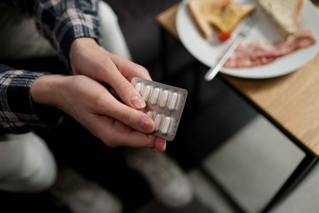 Hands holding a blister pack of tablets with breakfast on the table, a reminder to take ibuprofen for hemorrhoids with food
