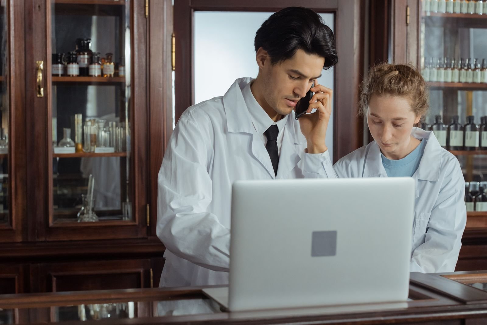 Pharmacist on a phone call beside a laptop, ready to check whether you can take a stool softener and use hemorrhoid cream together