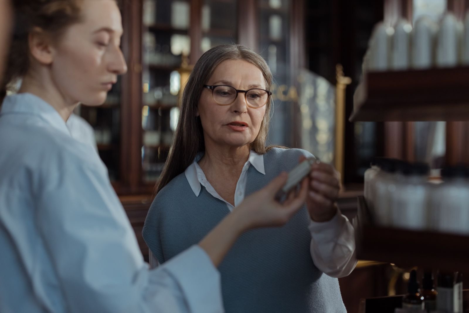 Pharmacist helping an older customer compare a cream vs ointment vs suppository at the pharmacy counter