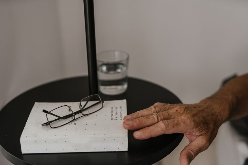 Elderly hand reaching toward a bedside table with a glass of water where a Senexon tablet might be taken at bedtime