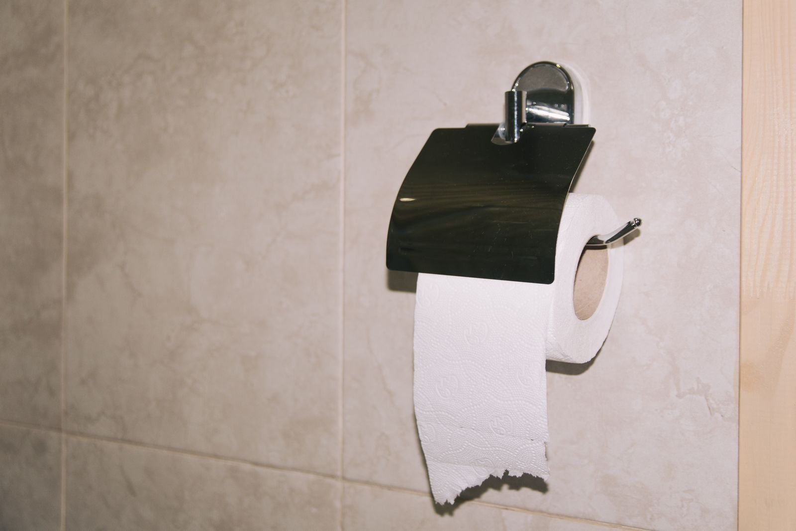 Toilet paper roll on a bathroom wall holder, showing the dry paper that Preparation H medicated wipes can replace