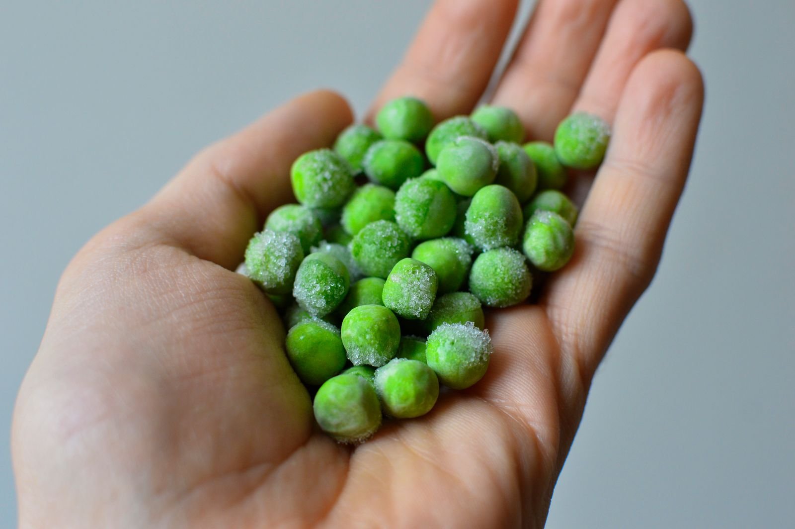 Hand holding frozen green peas, a flexible option when you need an ice pack for piles