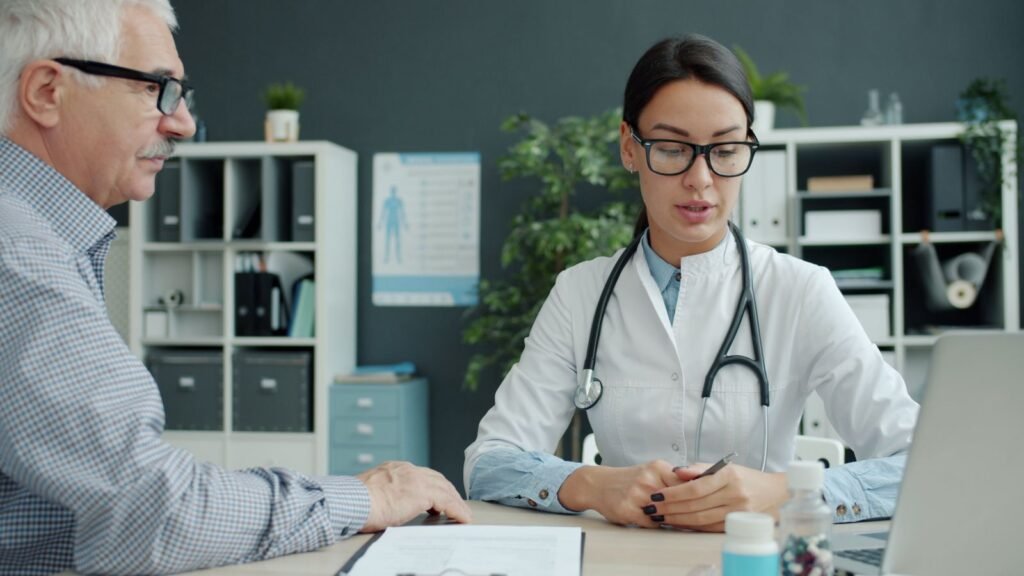 Doctor talking with an older man in an office, the kind of exam that sorts out hemorrhoids vs colorectal cancer warning signs