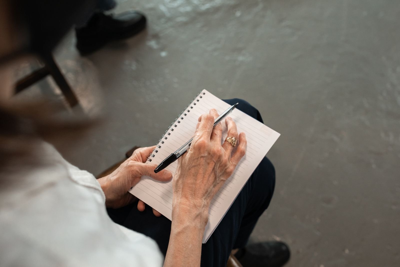 Older adult writing notes in a spiral notebook to track when hemorrhoids bleed before a doctor visit