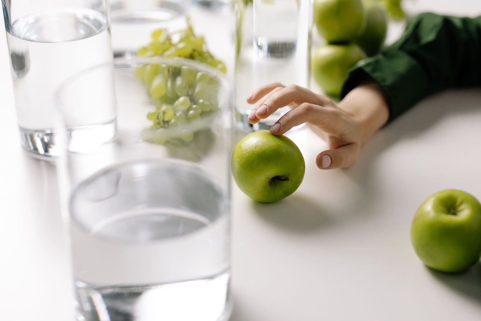 Glasses of water beside green apples and grapes, hydration and fiber that may help when hemorrhoids bleed